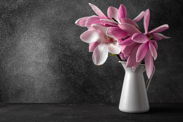 Stillleben mit rosa Magnolienblüten Strauß in Vase auf schwarzem Hintergrund. Hochzeits- oder Urlaubskonzept. Festlicher Hintergrund - Foto, Bild