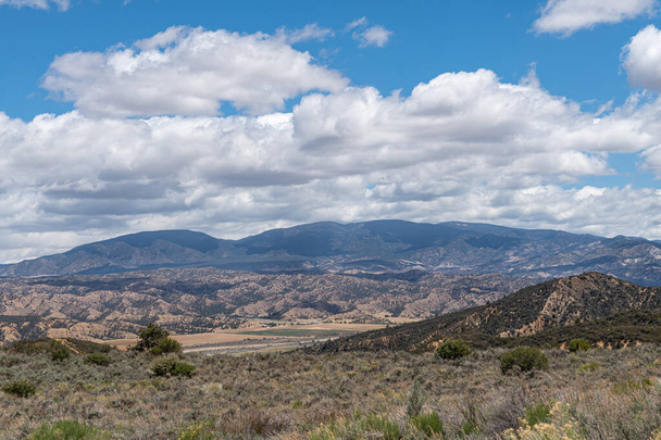 Las Narodowy Los Padres, CA, USA - 21 maja 2021: Suche pasmo górskie we wschodniej części pod błękitnym chmurowym krajobrazem z rolnictwem w dolinie. Roślinność krzewów. - Zdjęcie, obraz