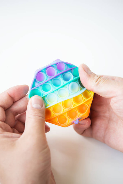 Nejmódnější senzorická hračka. Nová oblíbená barevná antistresová hračka ji vytlačí do tvaru šestiúhelníku v ruce. Fidget toy Rainbow Pop - Fotografie, Obrázek