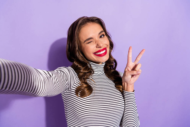 Self-portrait of attractive cheerful wavy-haired girl showing v-sign winking having fun isolated over bright violet purple color background - Fotografie, Obrázek