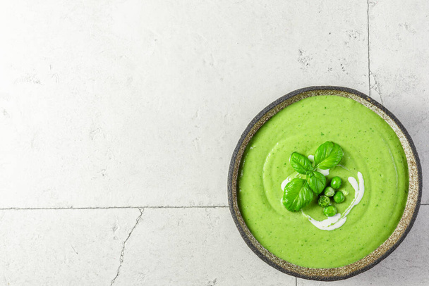Green pea cream soup in a bowl on light stone background. Top view with copy space. Healthy vegetarian food - Foto, Bild