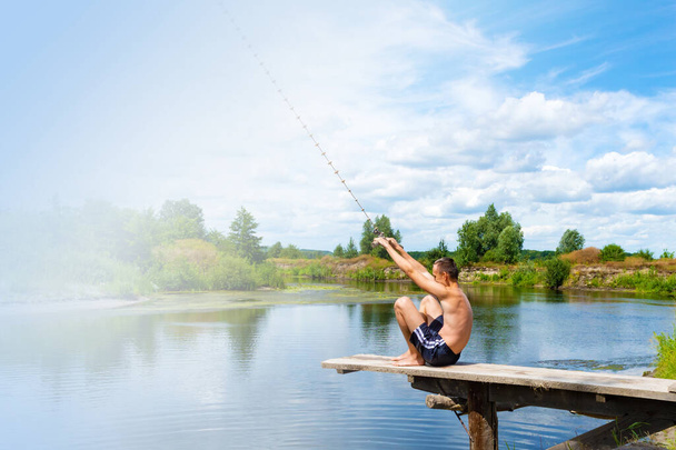 Niño adolescente se sienta en un puente de madera que va a saltar al río desde la cuerda oscilante en el día de verano soleado. Copiar espacio. - Foto, imagen