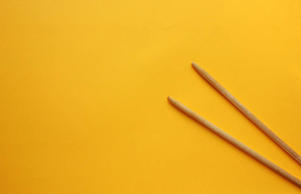 View from above on wooden chopsticks on a yellow background. Sticks are on the right side. Food appliances. Flat lay. Copy space. - Фото, изображение