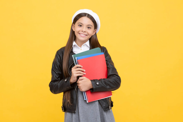 Okula dönen mutlu genç kız, sarı arka plan, eğitim kitaplarını tutuyor.. - Fotoğraf, Görsel