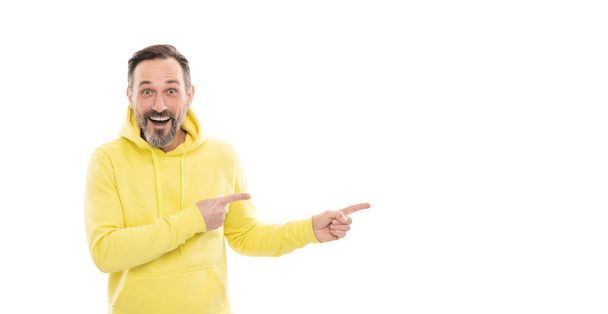 smiling senior guy presenting product isolated on white. advisor man in yellow hoody. adult guy advertising. male casual sporty fashion. copy space. mature surprised man pointing finger. - Photo, Image