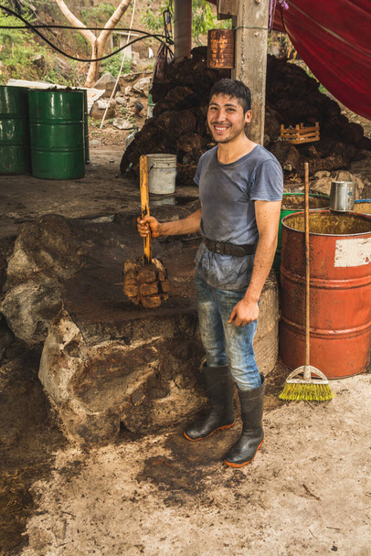 Mezcal master poaching for photography and smiling, in his right hand he carries a wooden mallet to crush the agave pineapples and extract the juice for the elaboration of mezcal - Photo, Image