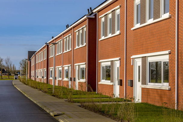 Gloednieuwe ontwikkeling van sociale woningbouw in een dorp in Nederland. Buurt scène van straat met moderne voorstedelijke rijtjeshuizen. - Foto, afbeelding