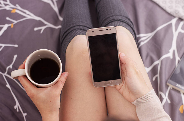 a woman looking at her mobile phone and drinking black coffee - 写真・画像