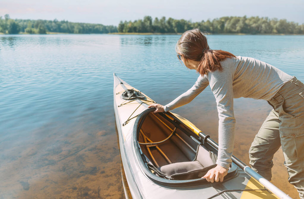 Young woman pushes a kayak in the water of lake on a summer sunny day. - 写真・画像