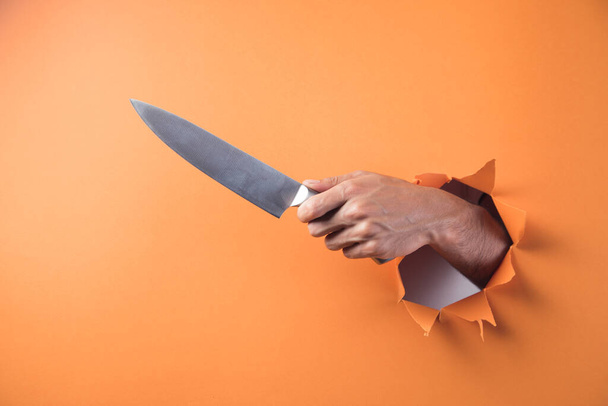 Hand holds knife on orange background - Photo, Image