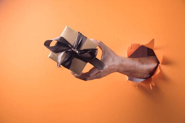 Hand hält Geschenkbox auf orangefarbenem Hintergrund - Foto, Bild