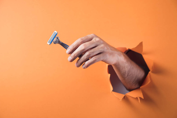 hand houdt een scheermes op een oranje achtergrond - Foto, afbeelding