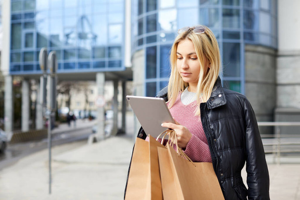 Mulher bonita nova com sacos de papel depois de fazer compras, segurando um tablet em suas mãos - Foto, Imagem