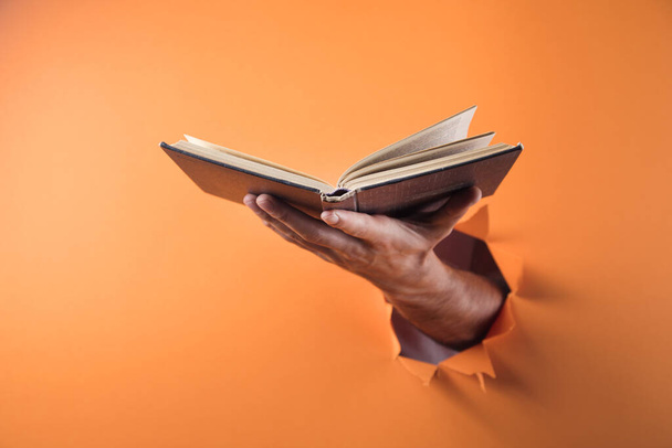 Hand holds book on orange background - Fotó, kép