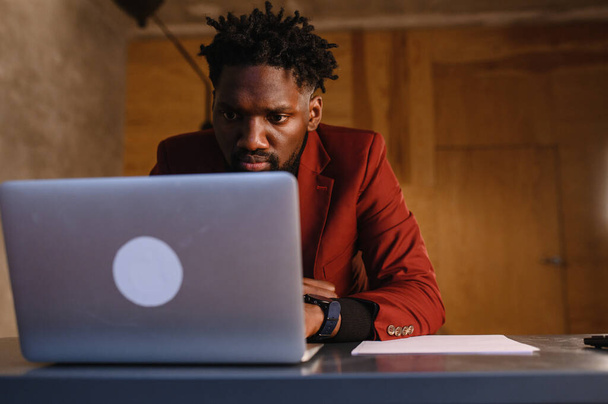 a focused black man in a suit is working on a laptop. Remote work from home - Fotoğraf, Görsel