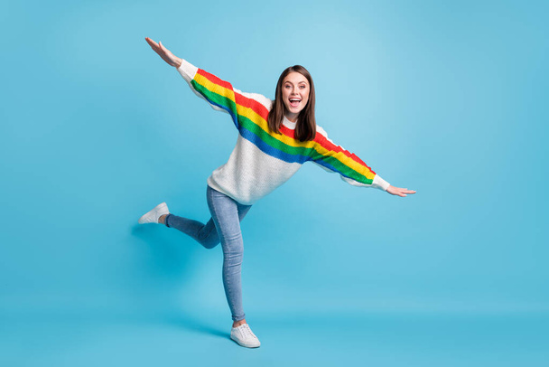 Full size photo of nice hooray brunette lady show plane wear colorful sweater jeans sneakers isolated on blue color background - Foto, Bild