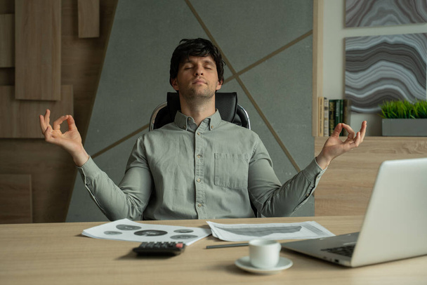 Man meditating in office coping with stress. Business executive doing yoga at desk in a modern office - Foto, imagen