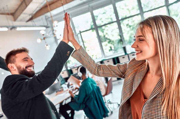 Successful coworker showing celebrating good results and giving high five in an office interior. Selective focus - 写真・画像