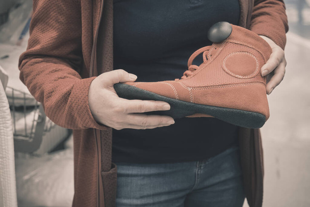 Γυναίκα στο κατάστημα επιλέγει να αγοράσει κόκκινα, μαλακά παπούτσια πυγμαχίας. Τα χέρια κοντά. - Φωτογραφία, εικόνα