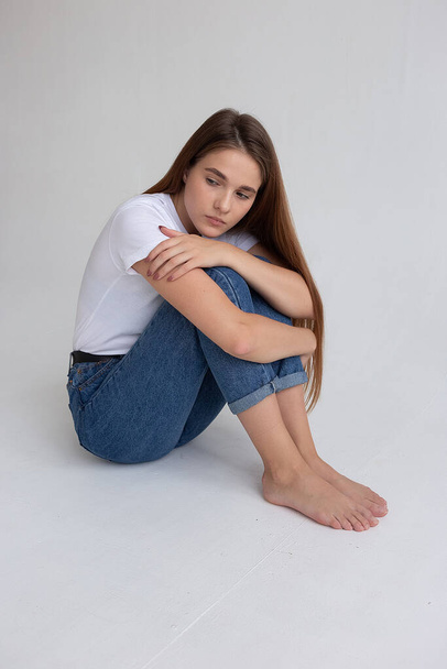 mladá běloška hezká dívka s dlouhými vlasy v tričku, modré džíny ve studiu - Fotografie, Obrázek