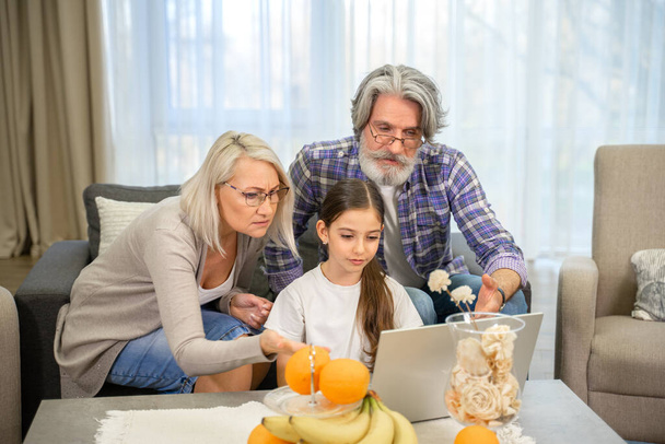 Nettes kleines Mädchen und ihre Großeltern schauen auf den Laptop-Bildschirm - Foto, Bild