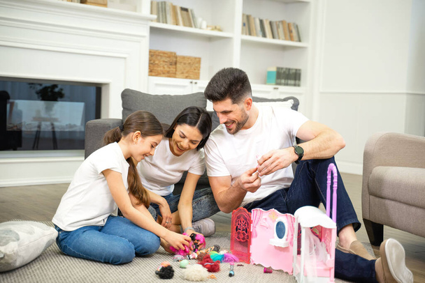 Usmívající se rodiče mají dobrý čas hrát si s dcerou a její domeček pro panenky - Fotografie, Obrázek