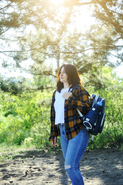 Smiling happy woman in yellow checkered shirt with a traveling bag spends time in the forest. Summer time holidays concept.  - Photo, Image