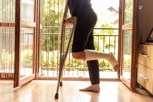 Close-up of a woman with a broken ankle, standing by the living room door - Foto, afbeelding