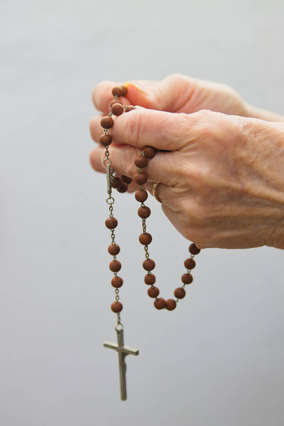 Close-up van de handen van een oudere vrouw met een christelijke rozenkrans met witte achtergrond - Foto, afbeelding