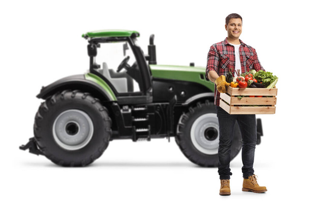 Farmer with a crate full of vegetables standing in front of a tractor isolated on white background - Fotó, kép