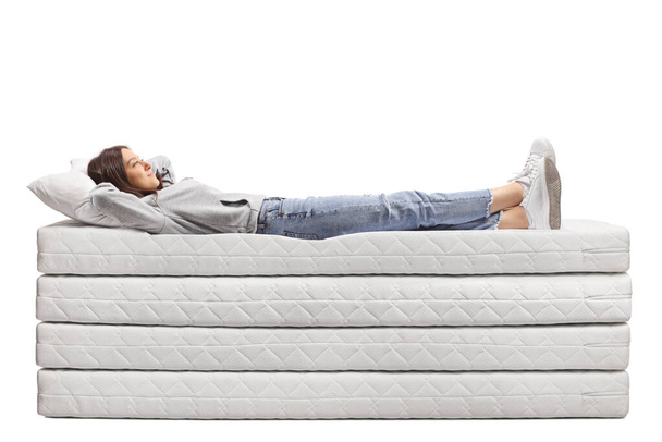 Full length shot of a young female in jeans laying on a pile of mattresses isolated on white background - Foto, immagini