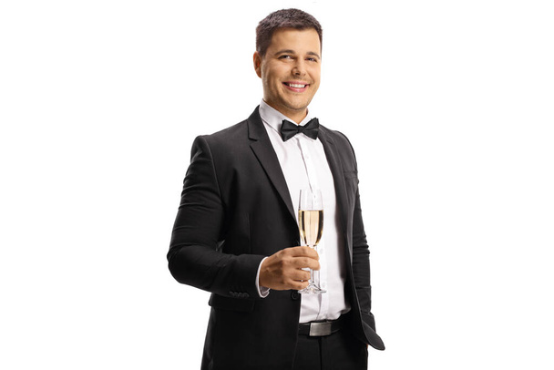 Young man in a suit and bow tie holding a glass of sparkling wine and looking at camera isolated on white background - 写真・画像