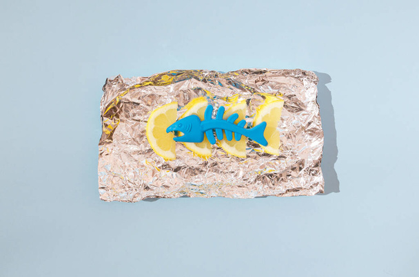 Ein blauer Plastikfisch und Zitronen auf einer Alufolie. Kreatives Sommer-Food-Konzept. Minimales zeitgenössisches Design. - Foto, Bild