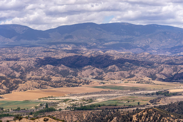 Los Padres National Forest, CA, USA - 21 mei 2021: Droge bergketen in oostelijk deel onder dik regenachtig wolkenlandschap met landbouwbedrijf in vallei. Sprlinkle donkergroene bomen. - Foto, afbeelding