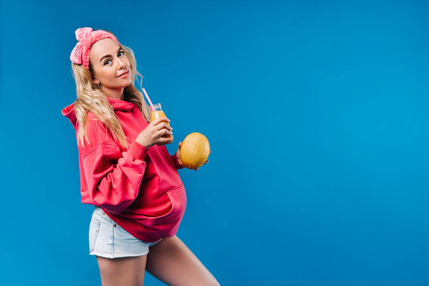pregnant girl in pink clothes with a bottle of juice and a melon on a blue background. - Foto, Imagem