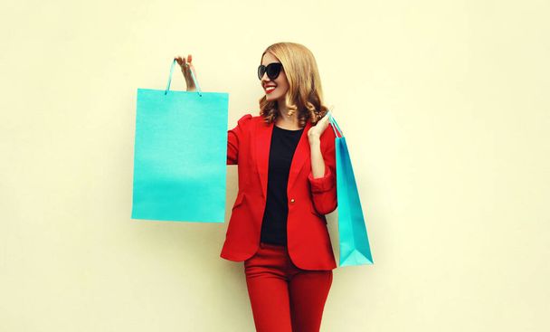 Portrait of happy smiling young woman with shopping bags wearing a red business blazer on a background - Фото, зображення