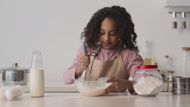 Linda niña afroamericana preparando masa para hornear, mezclando ingredientes con batidor en la cocina, cámara lenta - Metraje, vídeo