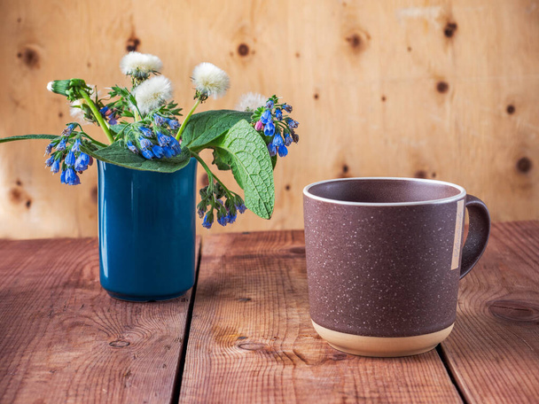Een kopje ochtendwafel in een grote bruine mok en een lenteboeket, paardebloemen en blauwe Symphytum caucasicum - Foto, afbeelding