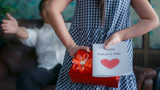 Little girl daughter holding and hiding greeting card for father behind back.Concept of Happy father's day - Photo, Image