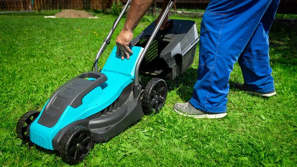 Rasenmähen. Arbeiter mähen Gras in einem grünen Hof. Ein Mann mit einem elektrischen Rasenmäher beim Rasenmähen. Gärtner beschneidet einen Garten - Foto, Bild