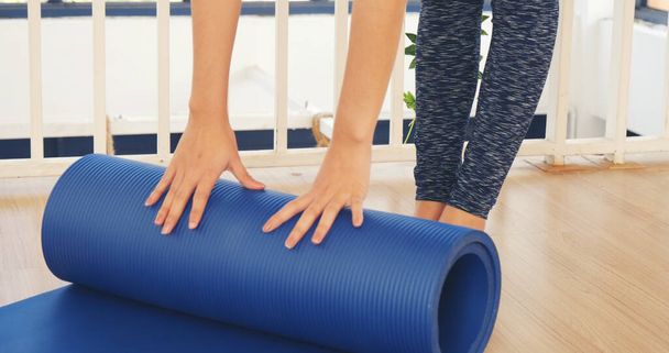 Vrouw handen opgerold yoga mat op sportschool vloer in yoga fitness trainingsruimte. Home workout vrouw close-up handen rollen schuim yoga gymnastiekmat. Vrouw blootsvoets thuis workout sportieve gezonde levensstijl concept - Foto, afbeelding