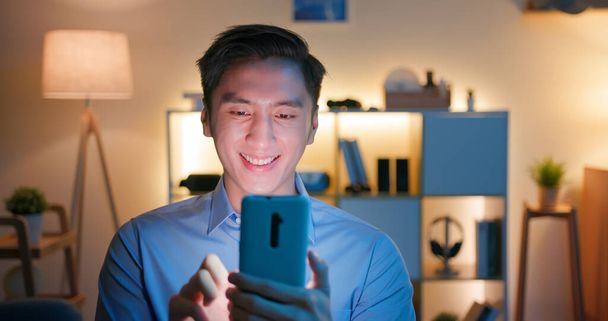 asian man use smart phone and watches something interesting on social media happily at home in the evening - Фото, изображение