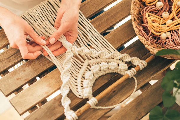 Close up of women's hands weaving macrame from white cotton threads in a home workshop.Home decor.Handmade concept.Selective focus with shallow depth of field,top view. - Foto, afbeelding