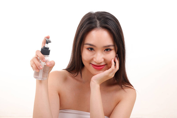 Kaunis nuori Kaakkois-Aasian nainen poseeraa tilalla käyttäen purista läpinäkyvä neste käsi sanitizer muovipullo aiheuttaa katso tarjous valkoinen tausta - Valokuva, kuva