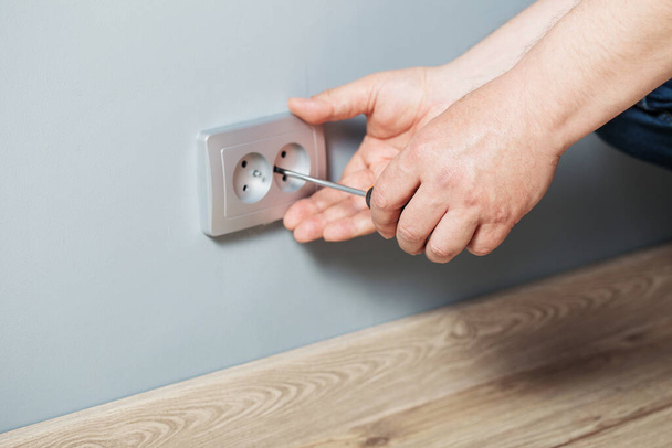 man installs an electrical outlet on gray wall - Foto, Imagem