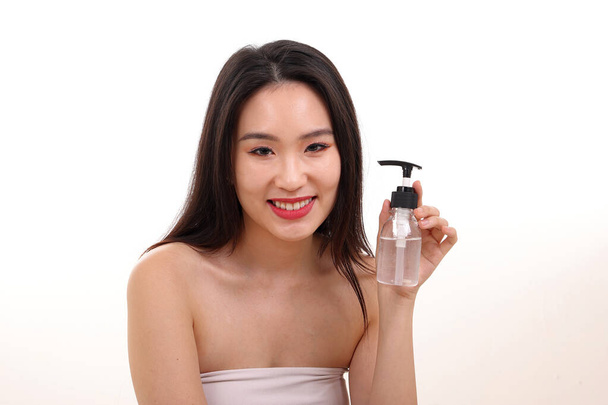 Hermosa joven mujer del sudeste asiático posando sosteniendo líquido transparente mano desinfectante plástico botella pose ver oferta fondo blanco sonrisa - Foto, imagen