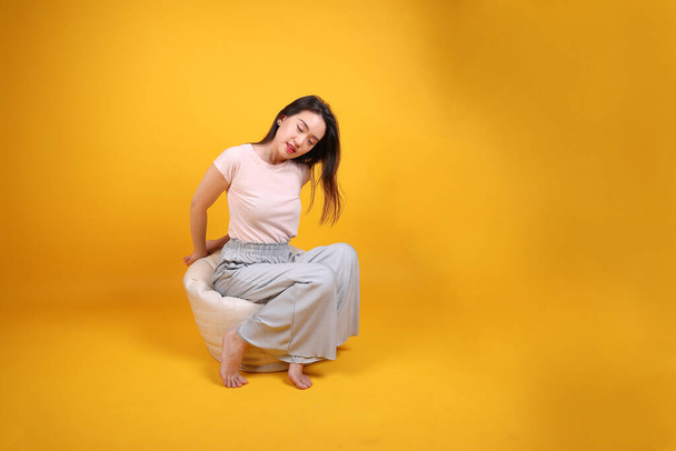 Красива молода жінка Південно-Східної Азії сидить на білому бірюзовому сидінні помаранчевий жовтий фон пози моди елегантний гарний настрій відпочинок відпочинку відпочиває подовжену йогу - Фото, зображення