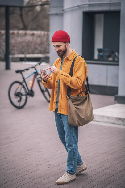 Man in a red hat and orange jacket with his smartphone in hands - Foto, immagini