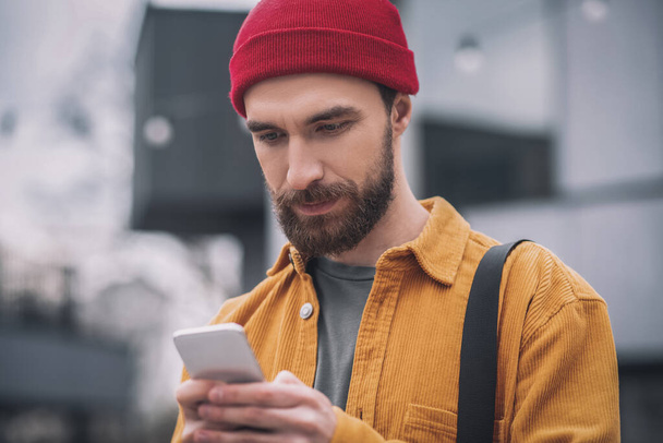 Man in a red hat holding his phone and texting a message - Photo, Image