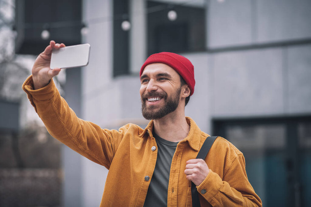 Uomo con un cappello rosso che tiene il telefono e fa selfie - Foto, immagini